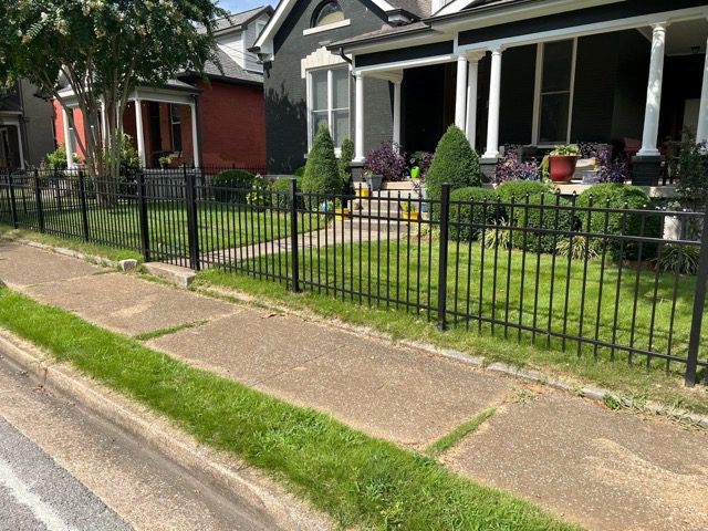 4' pressed point aluminum fence Black metal fence surrounding a suburban front yard with a house and garden.