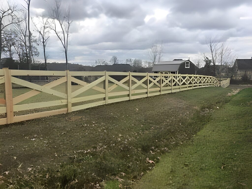 Wooden fence along grassy landscape under cloudy sky.