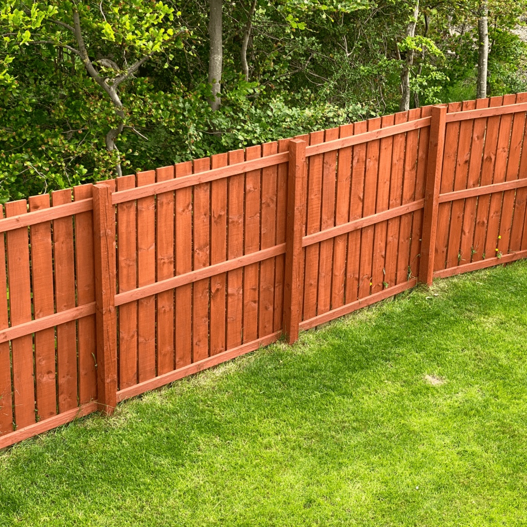 Red wooden fence beside green grass lawn.