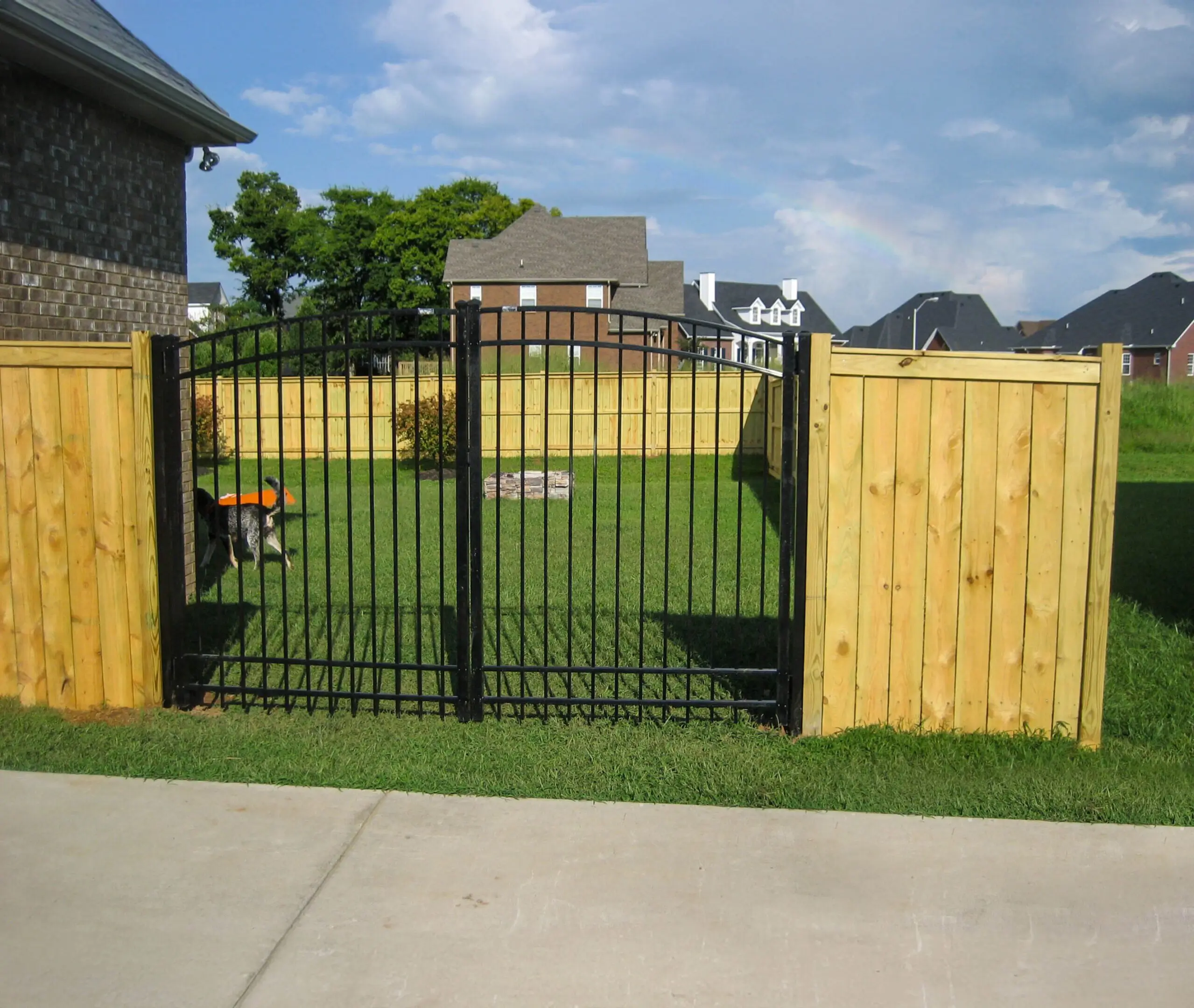Iron gate opening to fenced grassy yard.